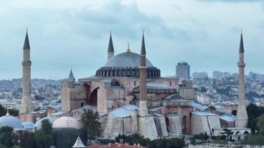 Establishing orbiting aerial drone shot of a Hagia Sophia Holy Grand Mosque with Bosphorus bridge and city skyline with a flag on the background in Fatih, Istanbul, Turkey at sunset. Cinematic footage