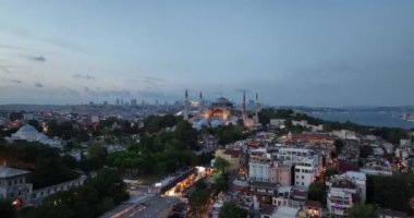 Establishing orbiting aerial drone shot of a Hagia Sophia Holy Grand Mosque with Bosphorus bridge and city skyline with a flag on the background in Fatih, Istanbul, Turkey at sunset. Cinematic footage