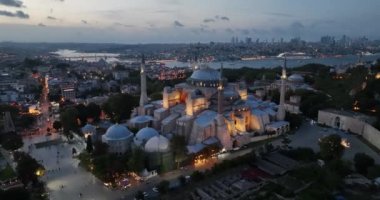 Establishing orbiting aerial drone shot of a Hagia Sophia Holy Grand Mosque with Bosphorus bridge and city skyline with a flag on the background in Fatih, Istanbul, Turkey at sunset. Cinematic footage