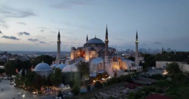 Establishing orbiting aerial drone shot of a Hagia Sophia Holy Grand Mosque with Bosphorus bridge and city skyline with a flag on the background in Fatih, Istanbul, Turkey at sunset. Cinematic footage