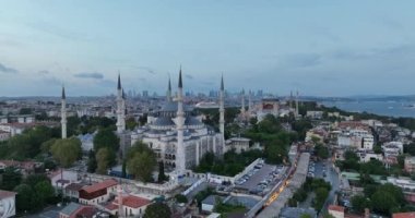 Establishing orbiting aerial drone shot of a Hagia Sophia Holy Grand Mosque with Bosphorus bridge and city skyline with a flag on the background in Fatih, Istanbul, Turkey at sunset. Cinematic footage