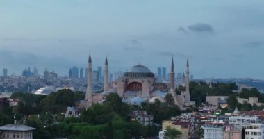 Establishing orbiting aerial drone shot of a Hagia Sophia Holy Grand Mosque with Bosphorus bridge and city skyline with a flag on the background in Fatih, Istanbul, Turkey at sunset. Cinematic footage