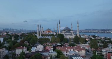 Establishing orbiting aerial drone shot of a Hagia Sophia Holy Grand Mosque with Bosphorus bridge and city skyline with a flag on the background in Fatih, Istanbul, Turkey at sunset. Cinematic footage