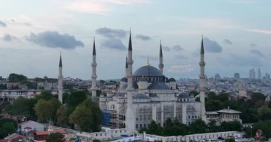 Establishing orbiting aerial drone shot of a Hagia Sophia Holy Grand Mosque with Bosphorus bridge and city skyline with a flag on the background in Fatih, Istanbul, Turkey at sunset. Cinematic footage