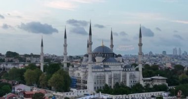 Establishing orbiting aerial drone shot of a Hagia Sophia Holy Grand Mosque with Bosphorus bridge and city skyline with a flag on the background in Fatih, Istanbul, Turkey at sunset. Cinematic footage