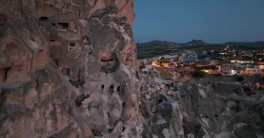 Aerial view of natural rock formations in the sunset, valley with cave houses in Cappadocia, Turkey. Natural landscape city lights at the night. Cinematic epic drone 4k hi quality footage.