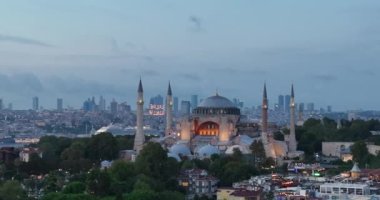 Establishing orbiting aerial drone shot of a Hagia Sophia Holy Grand Mosque with Bosphorus bridge and city skyline with a flag on the background in Fatih, Istanbul, Turkey at sunset. Cinematic footage