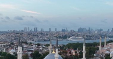 Establishing orbiting aerial drone shot of a Hagia Sophia Holy Grand Mosque with Bosphorus bridge and city skyline with a flag on the background in Fatih, Istanbul, Turkey at sunset. Cinematic footage