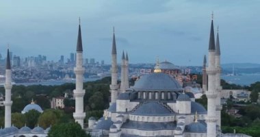 Establishing orbiting aerial drone shot of a Hagia Sophia Holy Grand Mosque with Bosphorus bridge and city skyline with a flag on the background in Fatih, Istanbul, Turkey at sunset. Cinematic footage