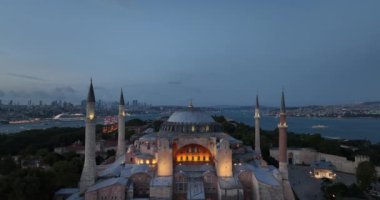 Establishing orbiting aerial drone shot of a Hagia Sophia Holy Grand Mosque with Bosphorus bridge and city skyline with a flag on the background in Fatih, Istanbul, Turkey at sunset. Cinematic footage