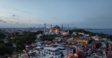 Establishing orbiting aerial drone shot of a Hagia Sophia Holy Grand Mosque with Bosphorus bridge and city skyline with a flag on the background in Fatih, Istanbul, Turkey at sunset. Cinematic footage