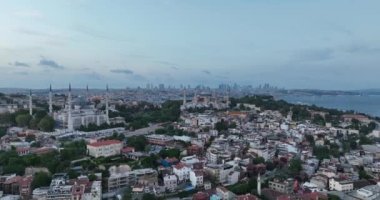 Establishing orbiting aerial drone shot of a Hagia Sophia Holy Grand Mosque with Bosphorus bridge and city skyline with a flag on the background in Fatih, Istanbul, Turkey at sunset. Cinematic footage