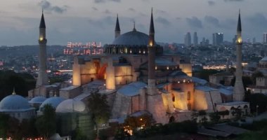Establishing orbiting aerial drone shot of a Hagia Sophia Holy Grand Mosque with Bosphorus bridge and city skyline with a flag on the background in Fatih, Istanbul, Turkey at sunset. Cinematic footage