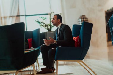 A modern businessman in a suit sits in a modern office and uses a smartphone. Selective focus. 