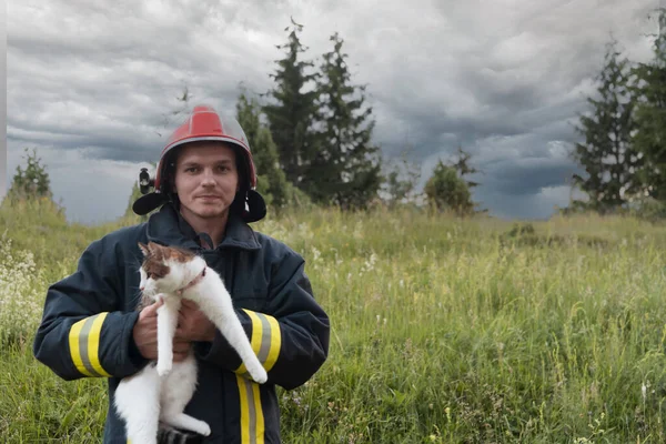 英雄的な消防士の保護服と赤いヘルメットのクローズアップ肖像は 彼の腕の中で保存猫を保持しています 消火活動中の消防士 高品質の写真 — ストック写真