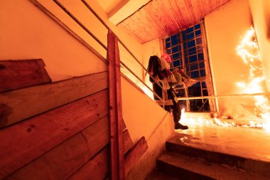 Cesur İtfaiyeci Yanan Binanın Merdivenlerinden İndi ve Kurtarılmış Kızı Kollarında Tuttu. Ateş açın ve arka planda bir itfaiyeci var. Yüksek kalite fotoğraf