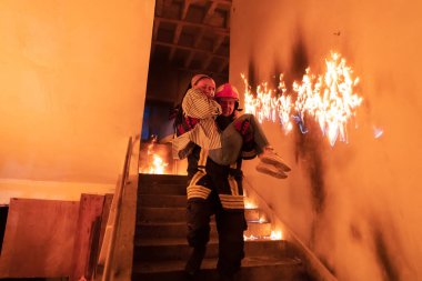 Cesur İtfaiyeci Yanan Binanın Merdivenlerinden İndi ve Kurtarılmış Kızı Kollarında Tuttu. Ateş açın ve arka planda bir itfaiyeci var. Yüksek kalite fotoğraf