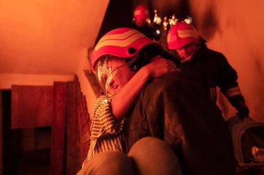 Cesur İtfaiyeci Yanan Binanın Merdivenlerinden İndi ve Kurtarılmış Kızı Kollarında Tuttu. Ateş açın ve arka planda bir itfaiyeci var. Yüksek kalite fotoğraf