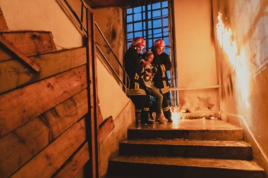 Cesur İtfaiyeci Yanan Binanın Merdivenlerinden İndi ve Kurtarılmış Kızı Kollarında Tuttu. Ateş açın ve arka planda bir itfaiyeci var. Yüksek kalite fotoğraf