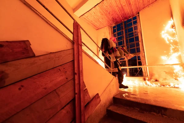 Cesur İtfaiyeci Yanan Binanın Merdivenlerinden İndi ve Kurtarılmış Kızı Kollarında Tuttu. Ateş açın ve arka planda bir itfaiyeci var. Yüksek kalite fotoğraf