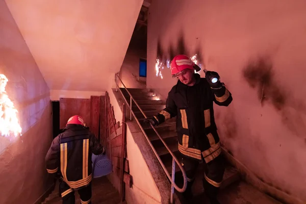 勇敢无畏的消防员从燃烧的大楼的楼梯上下来 并在他的怀里抱着一个被拯救的女孩 开火和一个消防员在后台 高质量的照片 — 图库照片