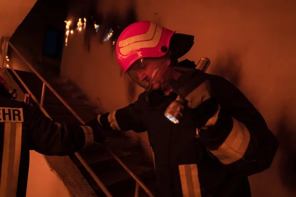 勇敢无畏的消防员从燃烧的大楼的楼梯上下来 并在他的怀里抱着一个被拯救的女孩 开火和一个消防员在后台 高质量的照片 — 图库照片
