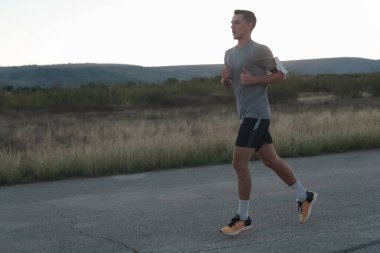 Çekici zinde bir adam gün batımında kırsal yolda hızla koşuyor, dışarıda koşuyor. Yüksek kalite fotoğraf