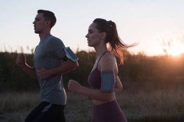 Sağlıklı genç bir çift sabahın erken saatlerinde arka planda güzel bir gündoğumuyla şehir sokaklarında koşuyor. Yüksek kalite fotoğraf