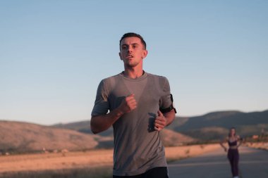 Sağlıklı genç bir çift sabahın erken saatlerinde arka planda güzel bir gündoğumuyla şehir sokaklarında koşuyor. Yüksek kalite fotoğraf