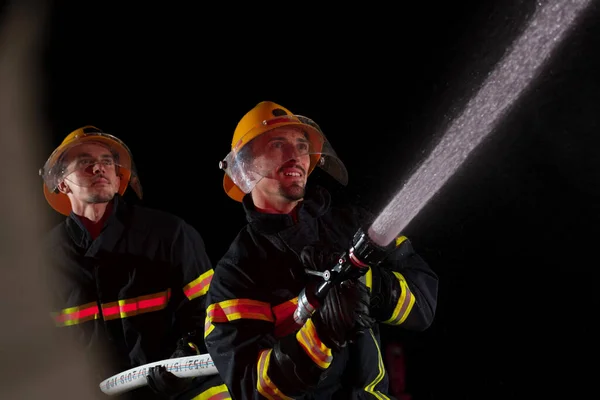 Firefighters use a water hose to eliminate a fire hazard. Team of firemen in the dangerous rescue mission. High quality photo