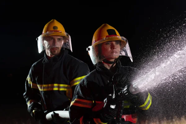 Firefighters using a water hose to eliminate a fire hazard. Team of female and male firemen in dangerous rescue mission. High quality photo