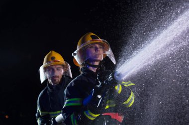 İtfaiyeciler yangın tehlikesini ortadan kaldırmak için su hortumu kullanıyorlar. Kadın ve erkek itfaiyeciler tehlikeli bir kurtarma görevinde. Yüksek kalite fotoğraf