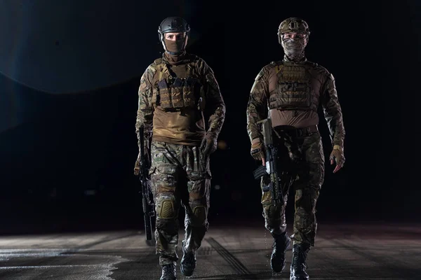 Heavily armed special forces soldiers in full protective military equipment with authentic assault rifles walking bravely and optimistic as winners from the war in night mission