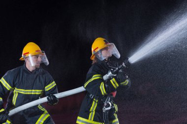 İtfaiyeciler yangın tehlikesini ortadan kaldırmak için su hortumu kullanıyorlar. Kadın ve erkek itfaiyeciler tehlikeli bir kurtarma görevinde. Yüksek kalite fotoğraf