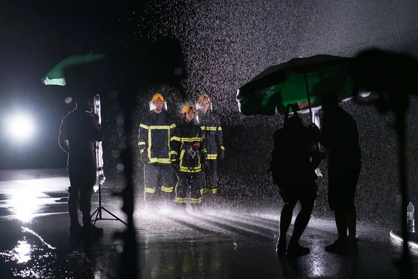 Behind the scene of Firefighters photo and cinema set with rain use a water hose to eliminate a fire hazard. Team of firemen in the rescue mission. High quality photo