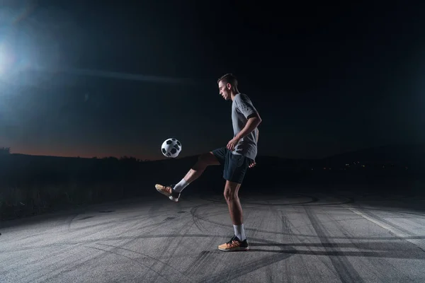 portrait of a young handsome talented soccer player man on a street playing with a football ball. High quality photo