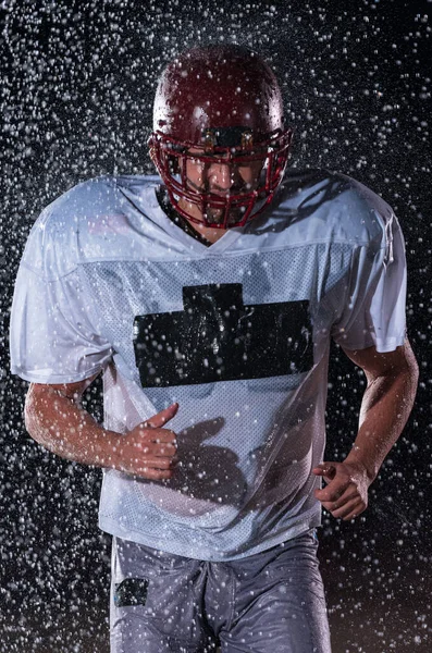 アメリカのサッカー選手戦士フィールドに立って彼のヘルメットを保持し 再生する準備ができて プレーヤータッチダウンを実行 およびスコアする準備をします 劇的なレンズフレアと雨滴と雨の夜 — ストック写真