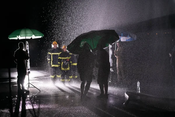 Behind the scene of Firefighters photo and cinema set with rain use a water hose to eliminate a fire hazard. Team of firemen in the rescue mission. High quality photo