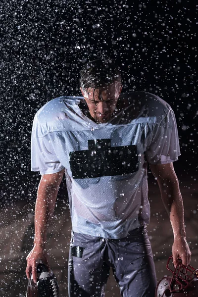 Premium Photo  American football athlete warrior standing on a field holds  his helmet and ready to play. player preparing to run, attack and score  touchdown. rainy night with dramatic lens flare