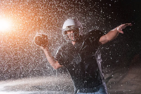 アメリカのサッカー選手戦士フィールドに立って彼のヘルメットを保持し 再生する準備ができて プレーヤータッチダウンを実行 およびスコアする準備をします 劇的なレンズフレアと雨滴と雨の夜 — ストック写真