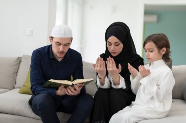 Geleneksel Müslüman ailelerin çocuklu aileleri, evde düzenlenen bir Ramazan ziyafeti sırasında iftar yemeğinden önce Kuran okuyup birlikte dua ediyorlar..