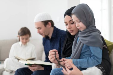 Geleneksel Müslüman ailelerin çocuklu aileleri, evde düzenlenen bir Ramazan ziyafeti sırasında iftar yemeğinden önce Kuran okuyup birlikte dua ediyorlar..
