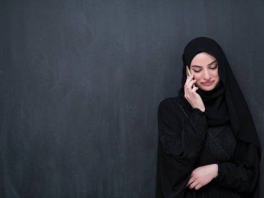 Genç, modern Müslüman iş kadınları siyah bir karatahtanın önünde tesettürlü kıyafetler giyerek akıllı telefon kullanıyorlar..