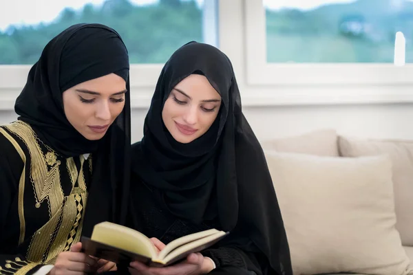 Young traditional Muslim women read Quran on the sofa before iftar dinner during a Ramadan feast at home. . High quality photo