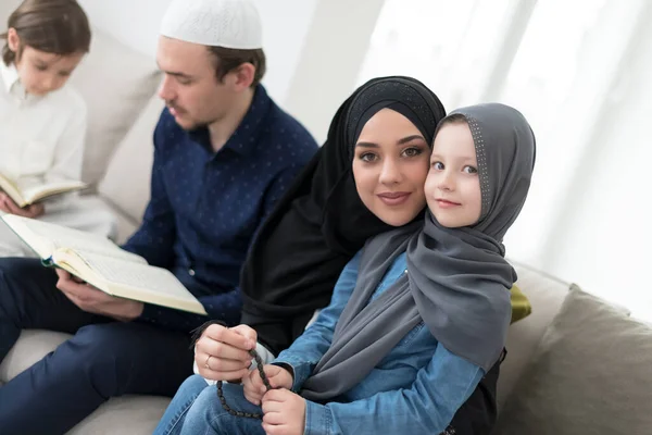 子供を持つ伝統的なイスラム教徒の家族はクルアーンを読み 自宅でラマダーンのごちそうの間にイフタールディナーの前にソファで一緒に祈る — ストック写真
