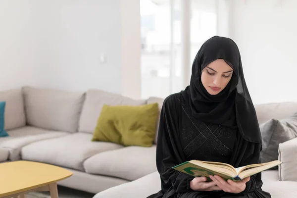 Young traditional Muslim women read Quran on the sofa before iftar dinner during a Ramadan feast at home.