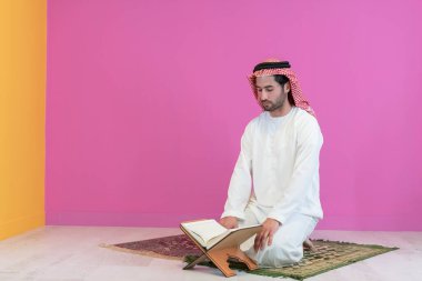 Geleneksel giysiler içinde genç Arap Müslüman bir adam evde bir Ramazan Bayramı ziyafeti sırasında iftar yemeğinden önce kutsal halıda Kuran okuyor. Yüksek kalite fotoğraf