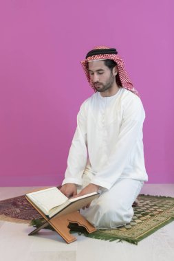Geleneksel giysiler içinde genç Arap Müslüman bir adam evde bir Ramazan Bayramı ziyafeti sırasında iftar yemeğinden önce kutsal halıda Kuran okuyor. Yüksek kalite fotoğraf