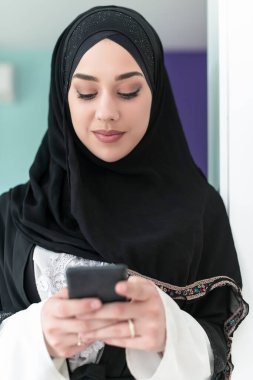 Genç, modern Müslüman iş kadınları evde geleneksel tesettürlü kıyafetler giymek için akıllı telefon kullanıyorlar. Yüksek kalite fotoğraf