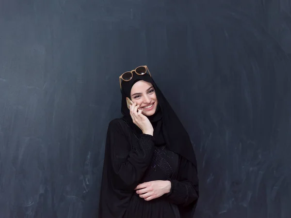 黒の黒板の前にサングラスとヒジャーブの服を着たスマートフォンを使っている若い現代のイスラム教徒の実業家 高品質の写真 — ストック写真